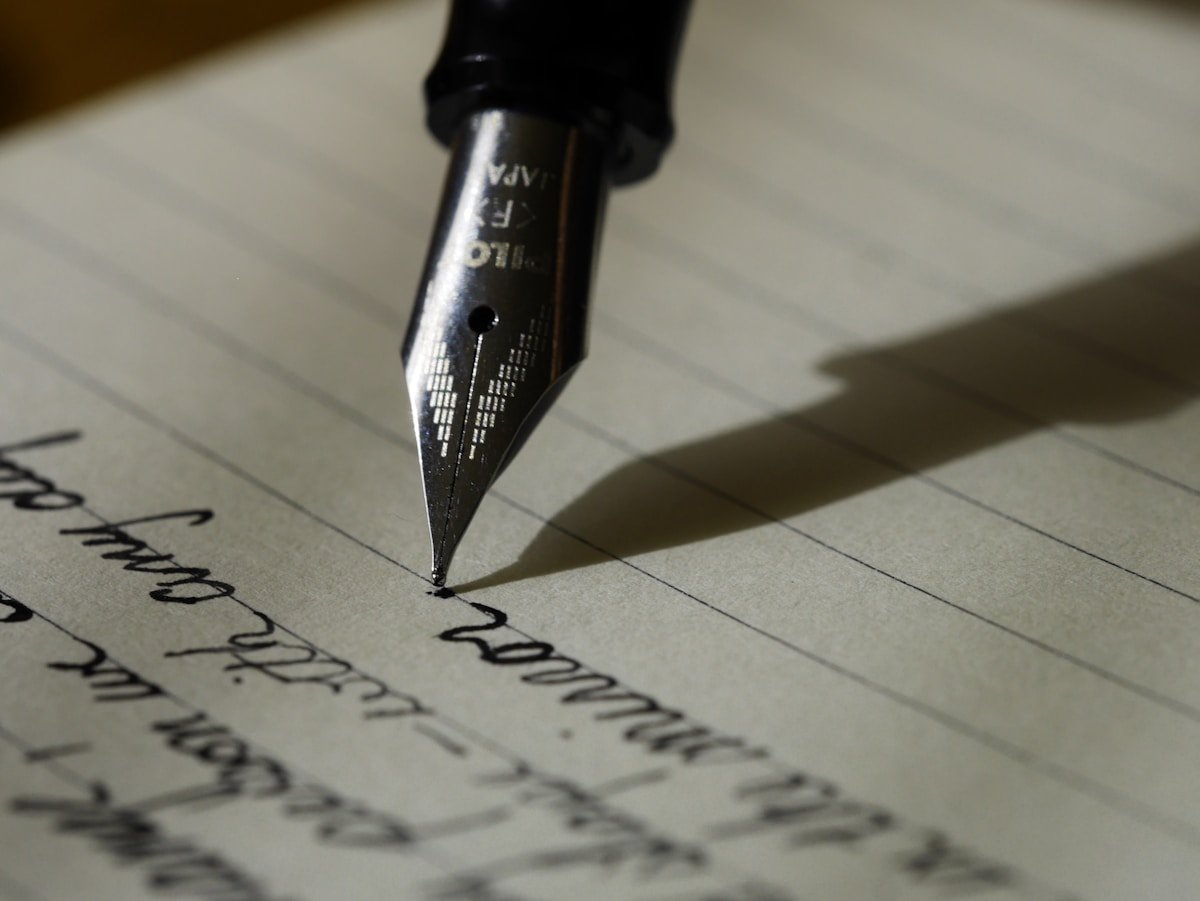 Mão escrevendo em caderno, close no papel com letras, fundo desfocado e aconchegante