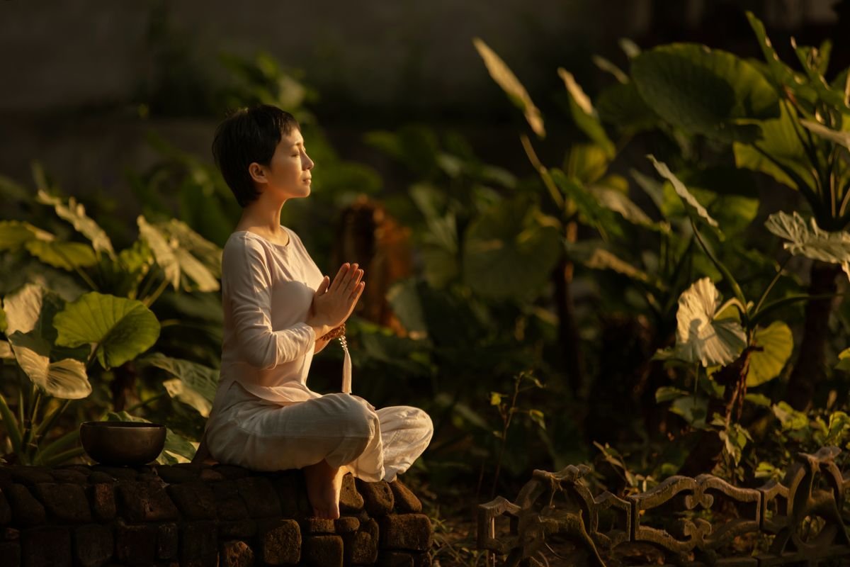 Pessoa em meditação ao amanhecer, ambiente tranquilo, luz suave, postura relaxada mas atenta